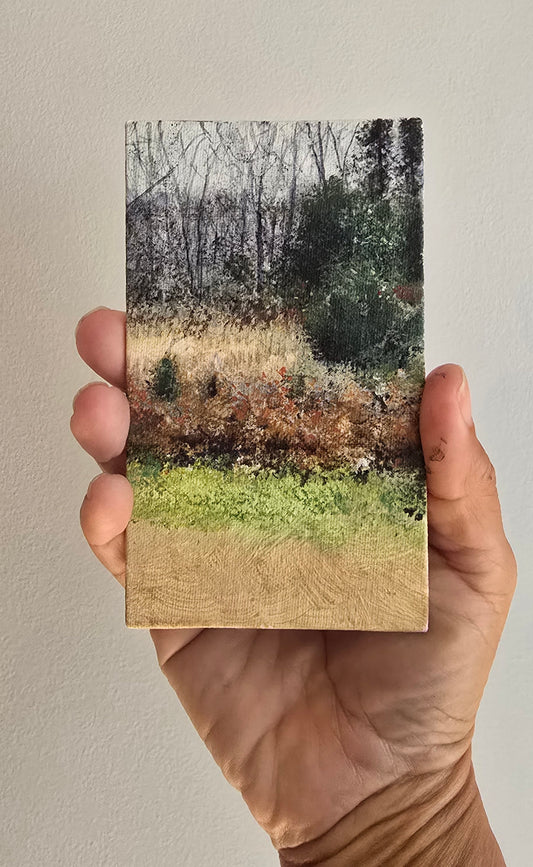 Hand holding a rectangular card with a nature scene of trees and grass.