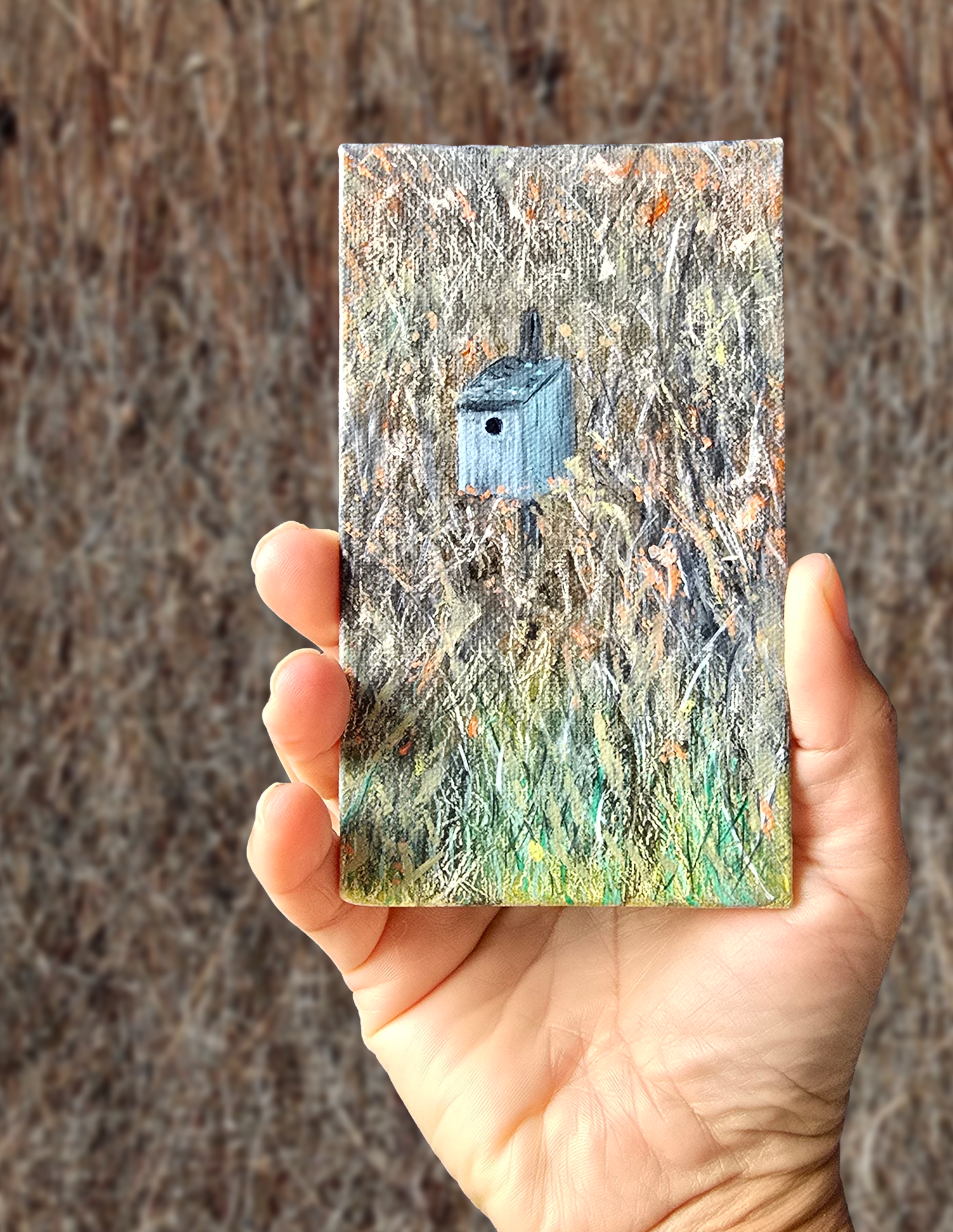 Hand holding a small rectangular object with a nature-themed design against a textured brown background