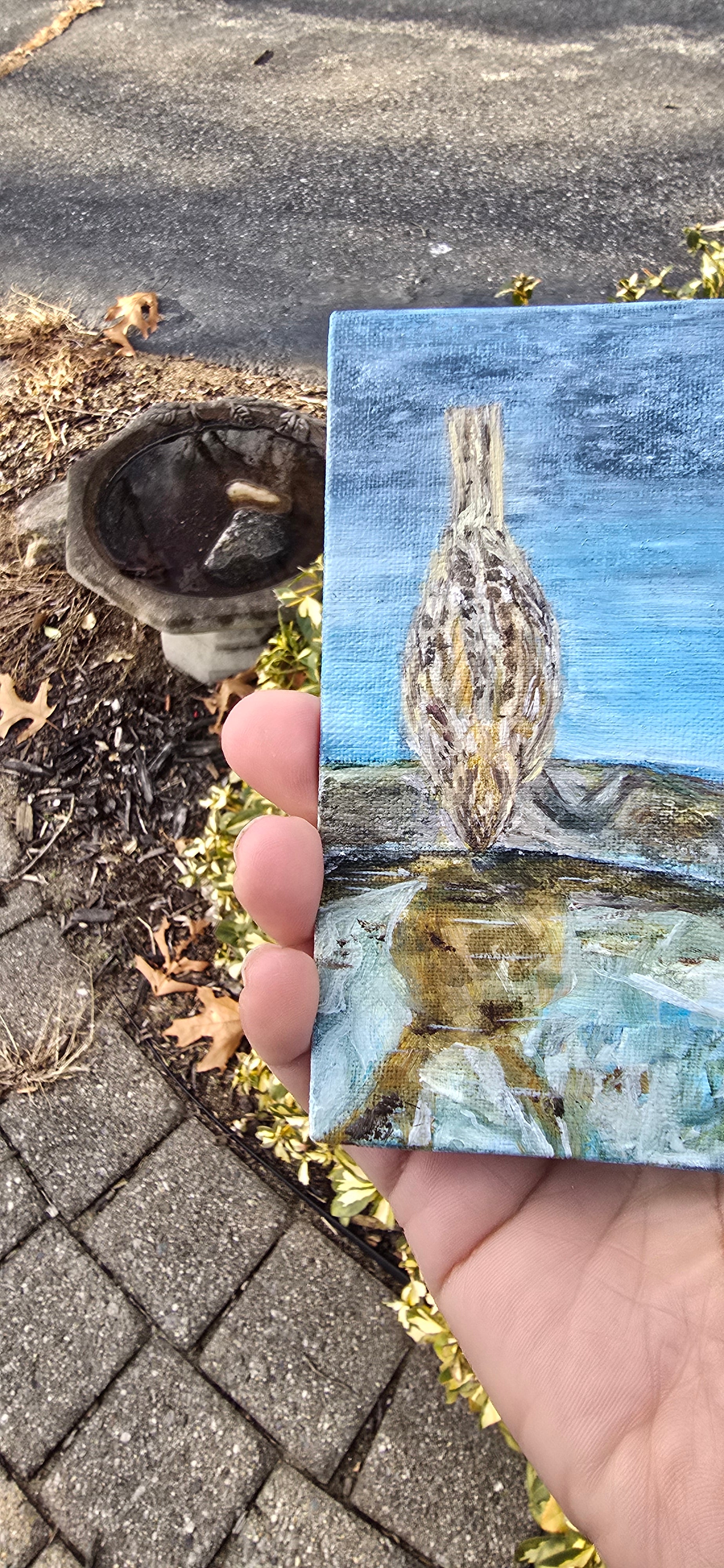 Small painting of a bird held between fingers on a textured surface