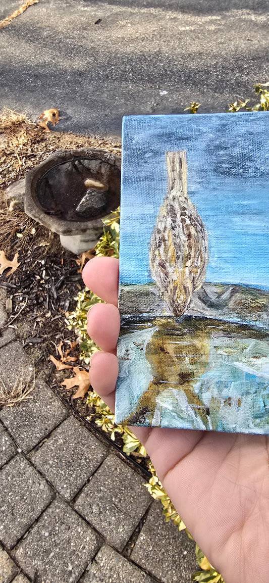Small painting of a bird held between fingers on a textured surface