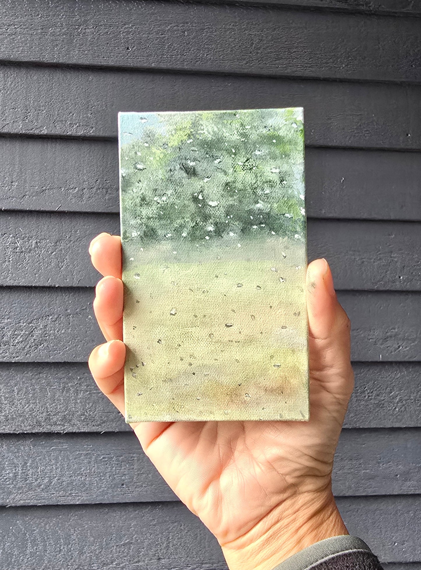 Hand holding a rectangular stone sample with a textured surface against a dark background