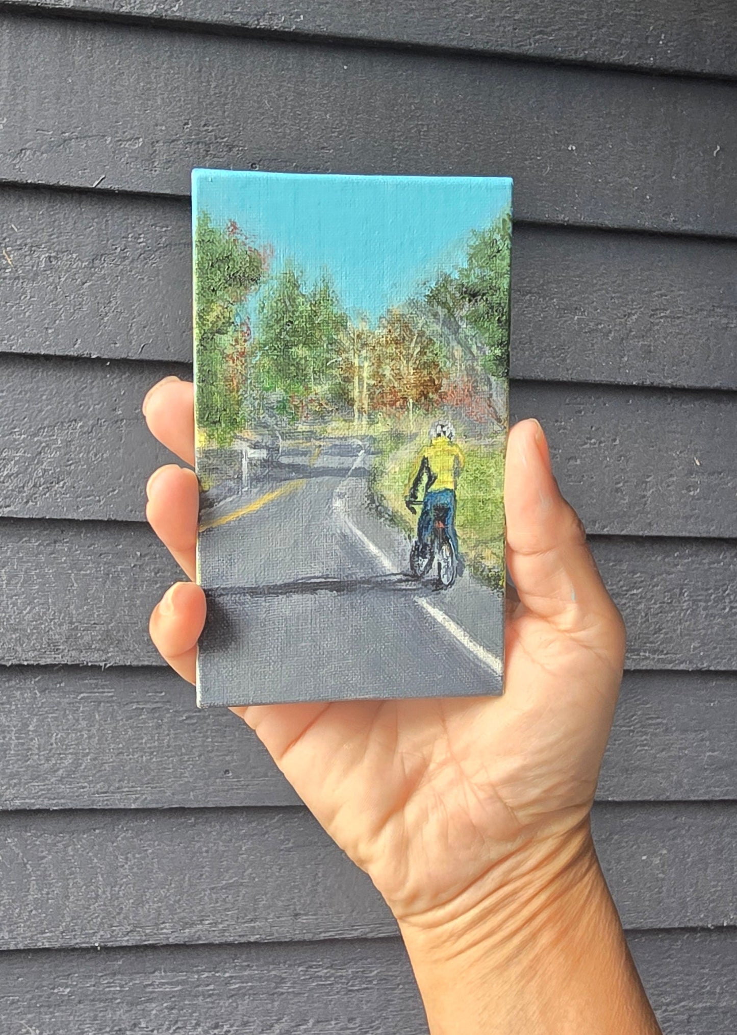 Hand holding a small postcard with a scenic view on a textured gray surface