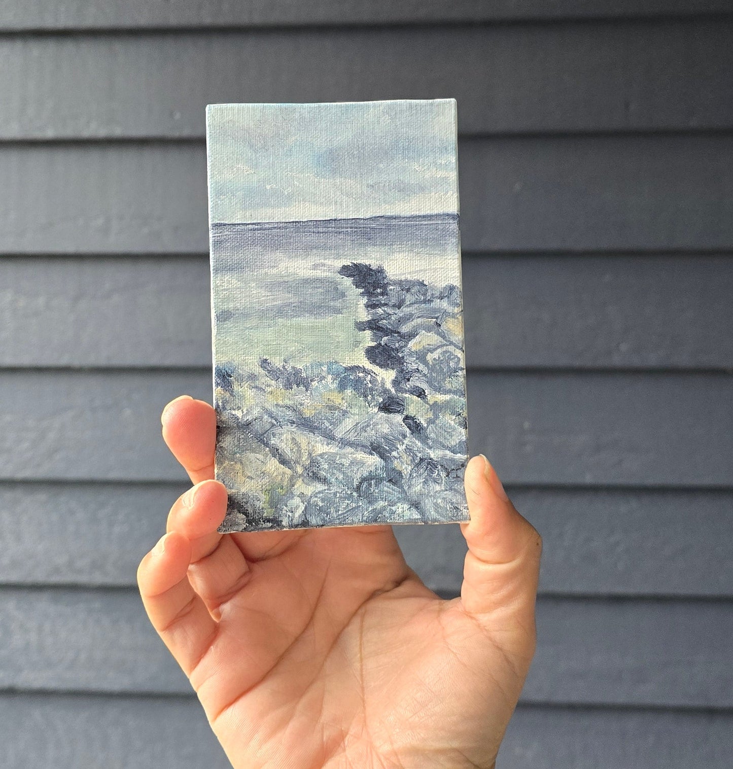 Hand holding a small rectangular sample of blue and gray marble against a dark background
