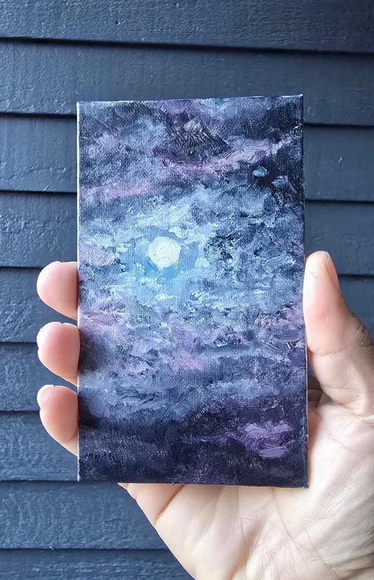 Hand holding a rectangular piece of purple stone with a white center against a dark wooden background